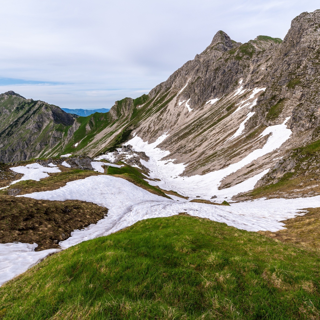 Снег на склонах горы с зеленой травой 