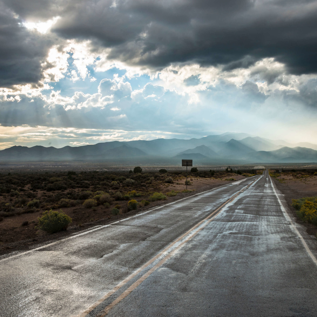 Мокрая дорога в лучах солнца под пасмурным небом 