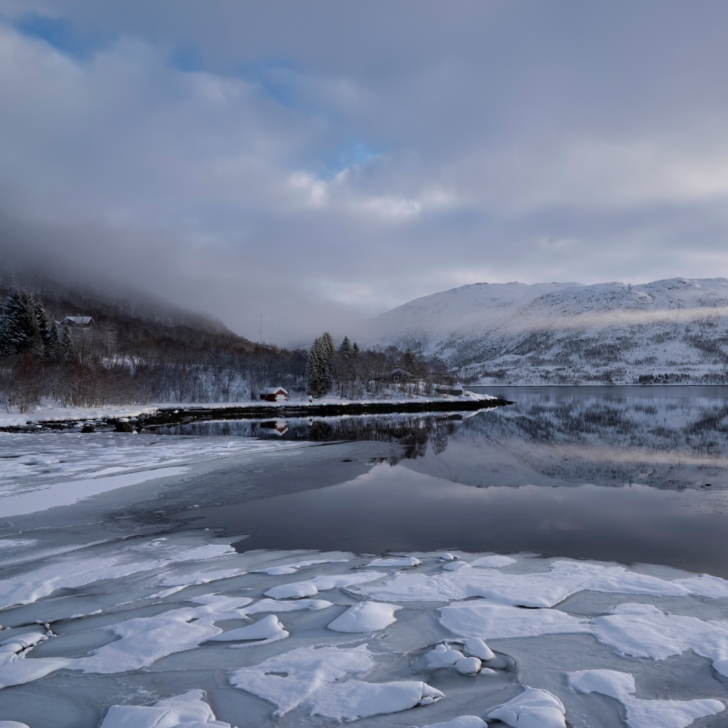 Покрытое льдом холодное озеро у гор в тумане