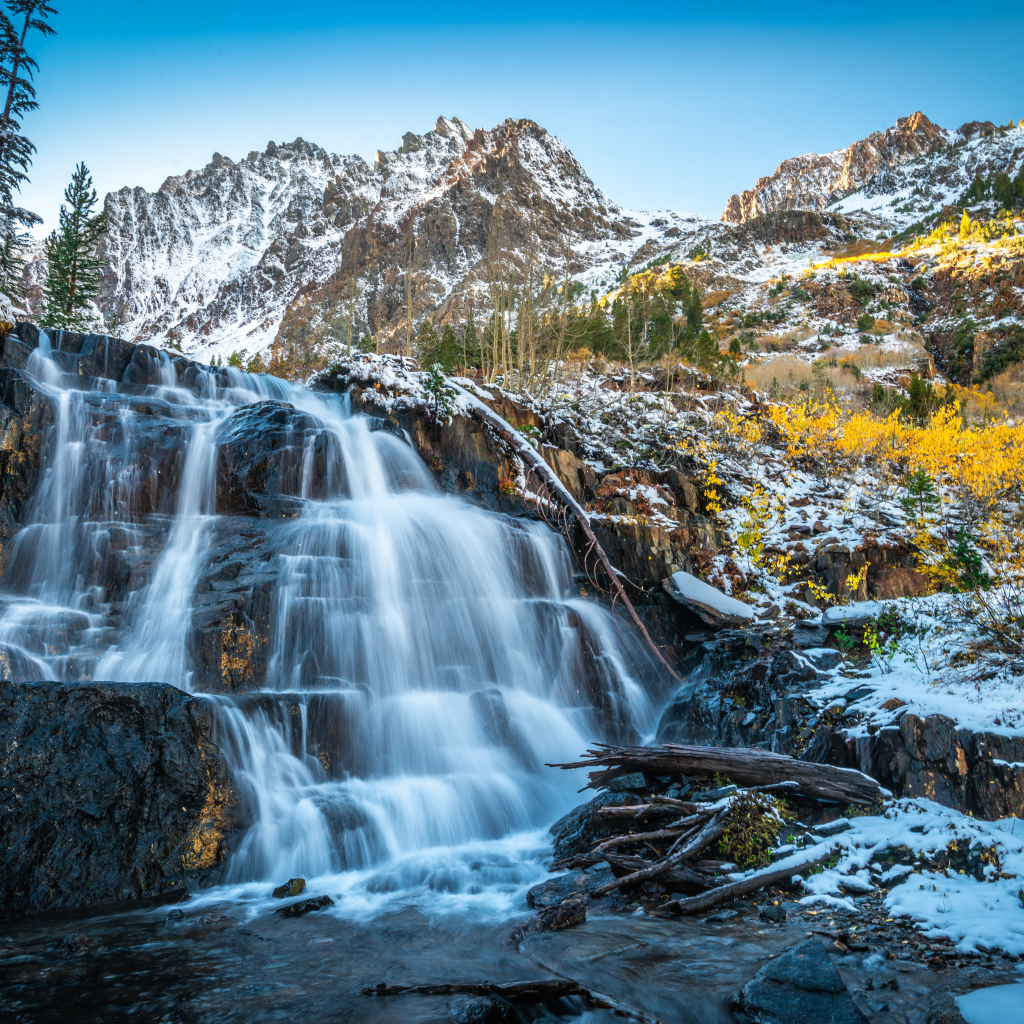 Красивый водопад стекает по холодным камням на фоне заснеженных гор