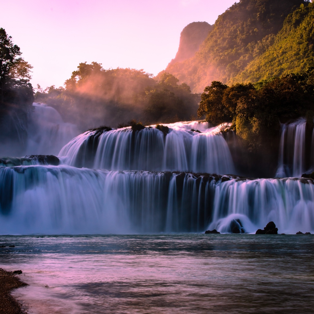 Каскадный водопад стекает по камням в лучах солнца 