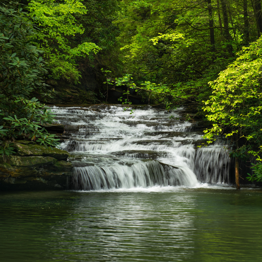Водопад стекает по каменному каскаду в реку 