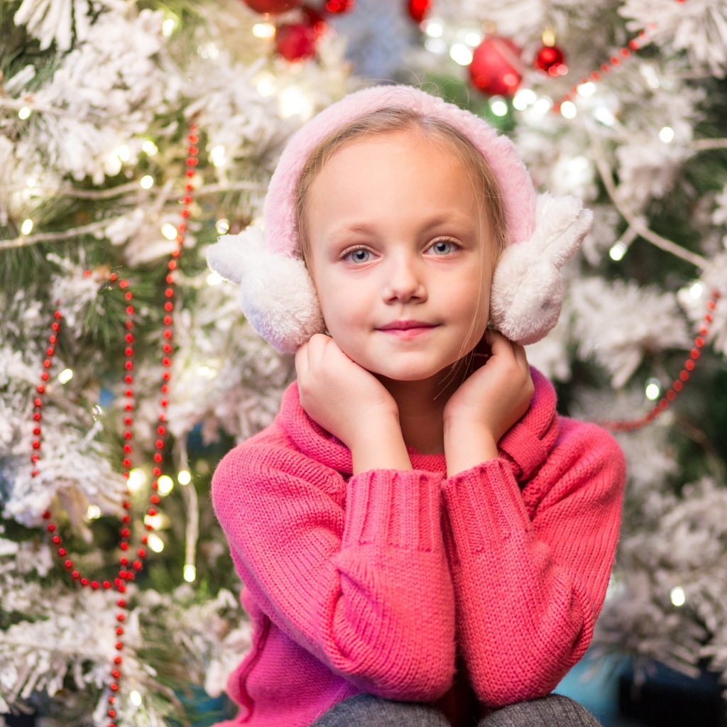 Девочка в розовых наушниках сидит у ели