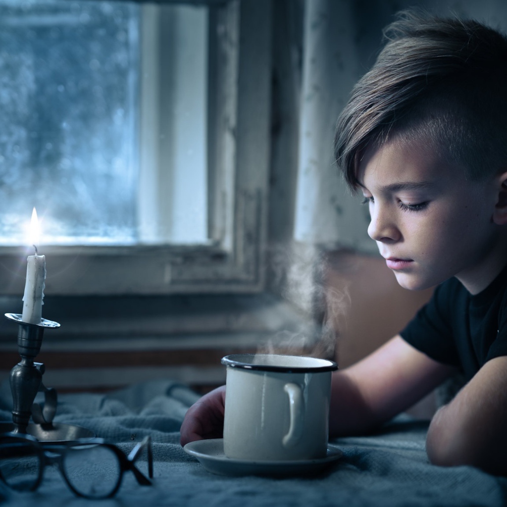 Маленький мальчик сидит за столом при свете свечи 
