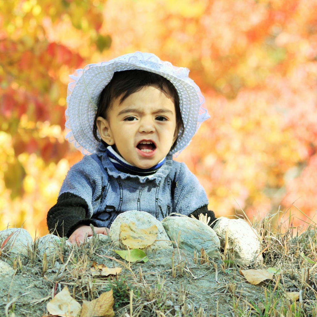 Маленькая девочка в шляпке сидит на земле