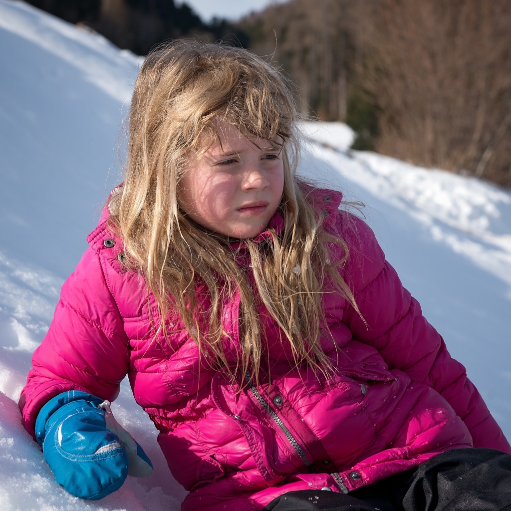 Маленькая девочка лежит на заснеженной горке 