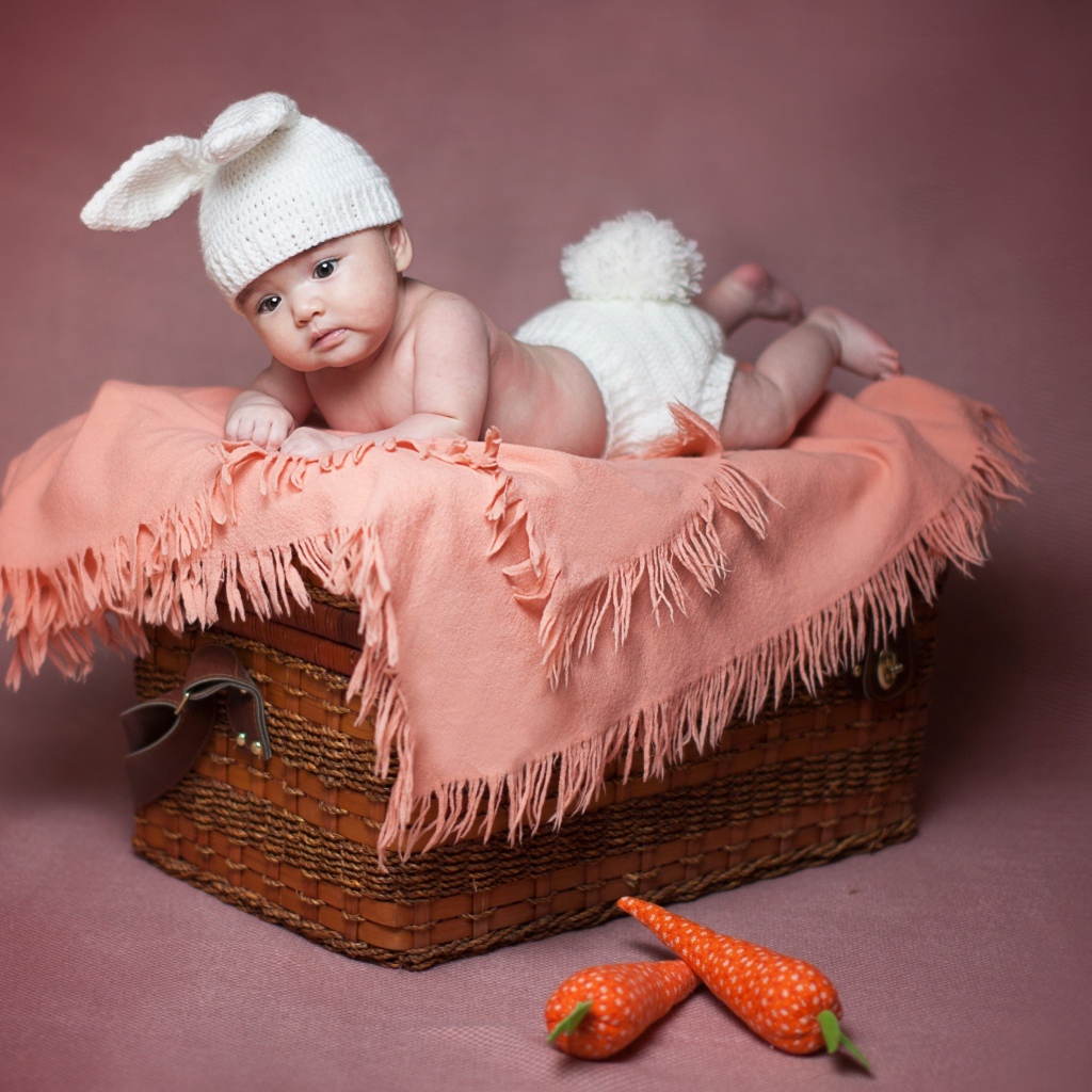 Маленький ребенок в костюме зайчика лежит на корзине 