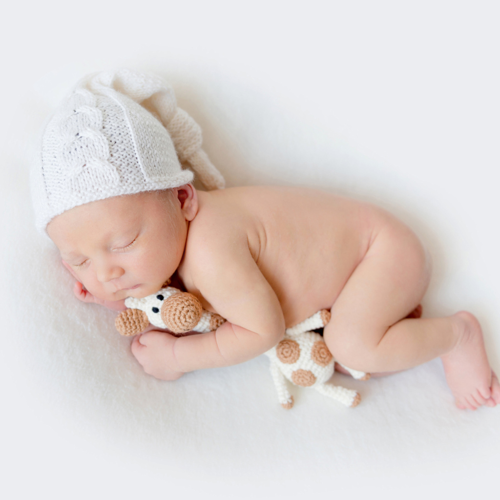 Младенец в шапке с игрушкой на белом фоне