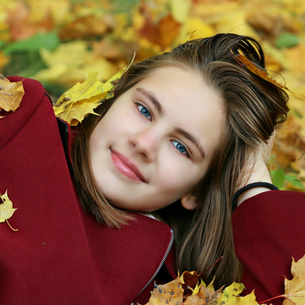 Красивая голубоглазая девочка лежит на опавшей листве