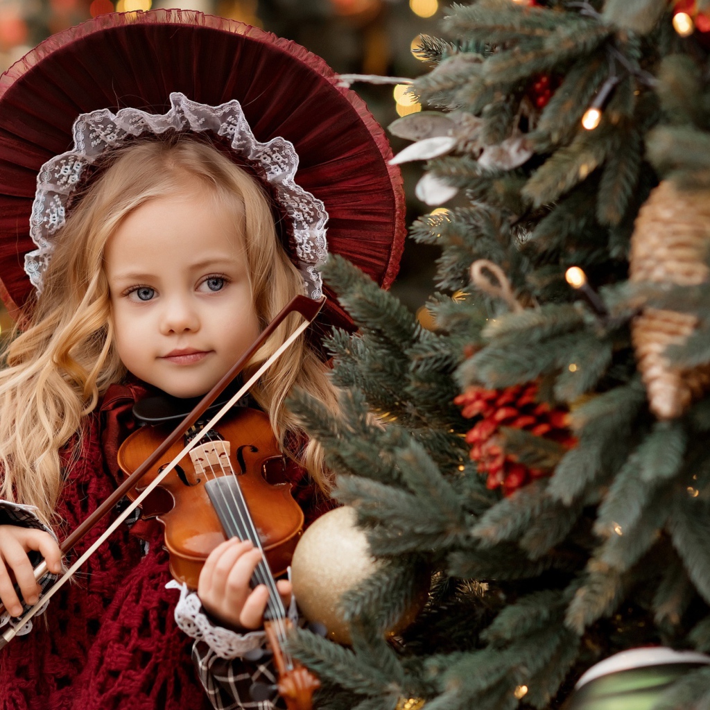 Красивая маленькая девочка со скрипкой у ели
