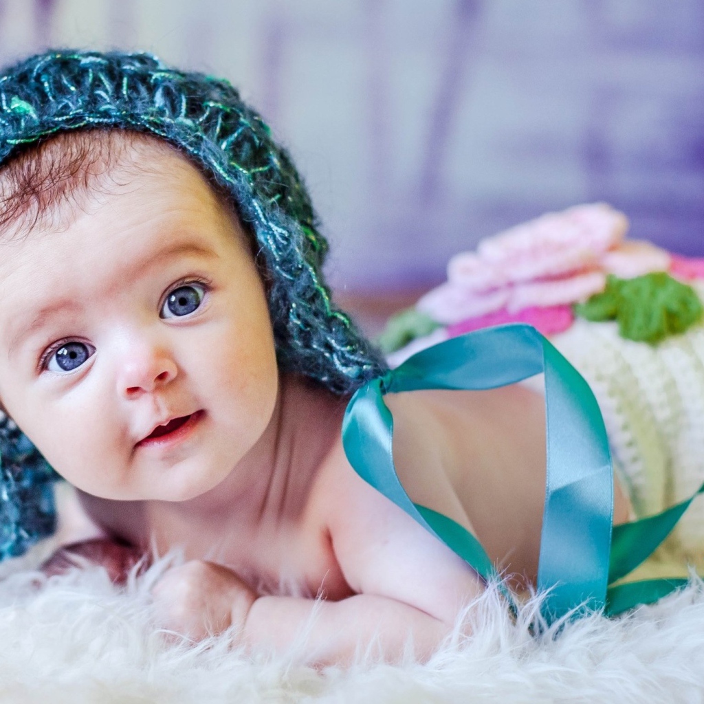 Голубоглазая маленькая девочка в вязаной шапке с ленточками