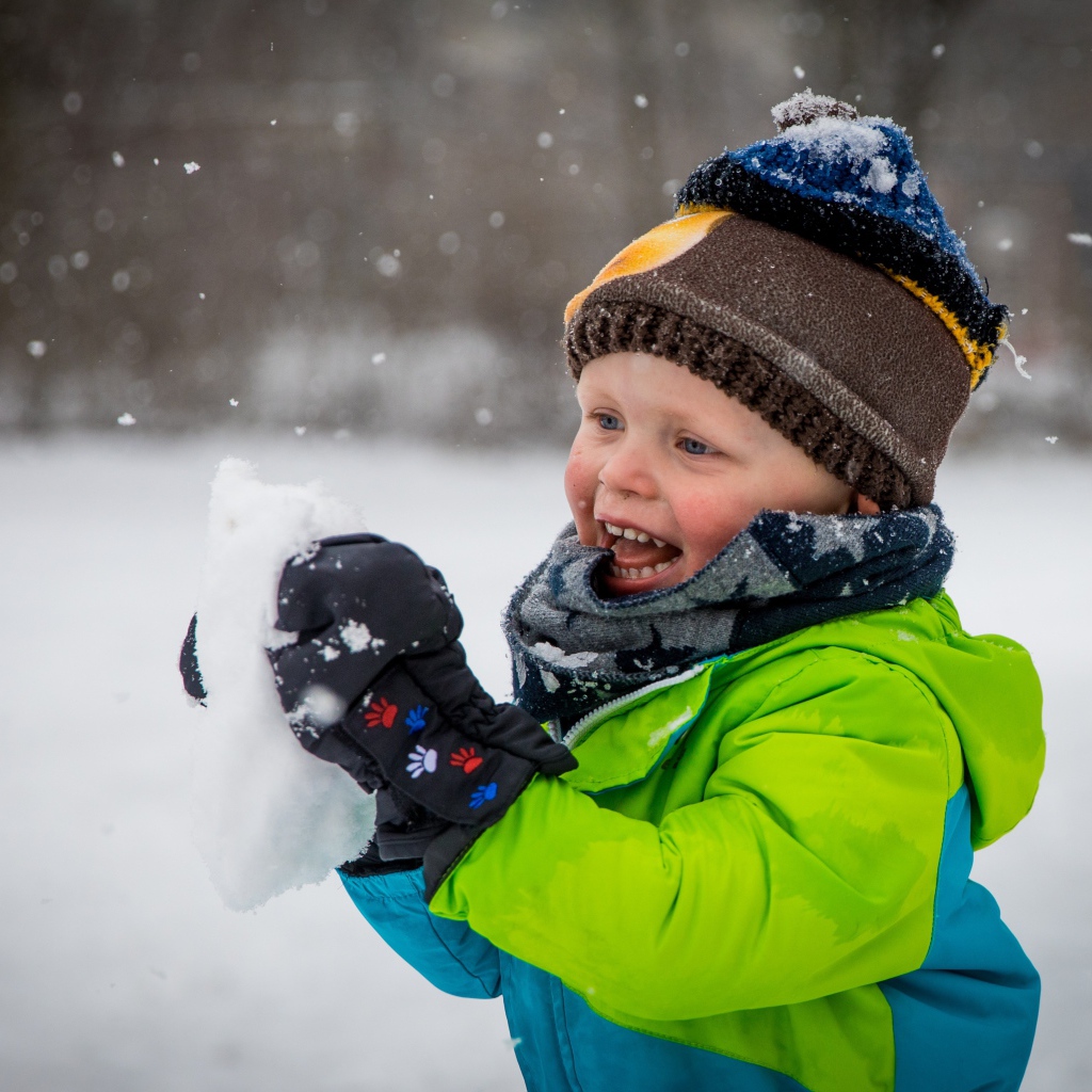 Веселый маленький мальчик со снегом в руках 