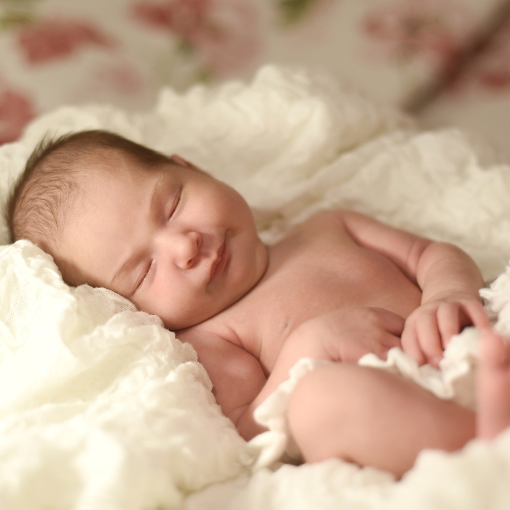 Милый грудной ребенок спит на белом покрывале 