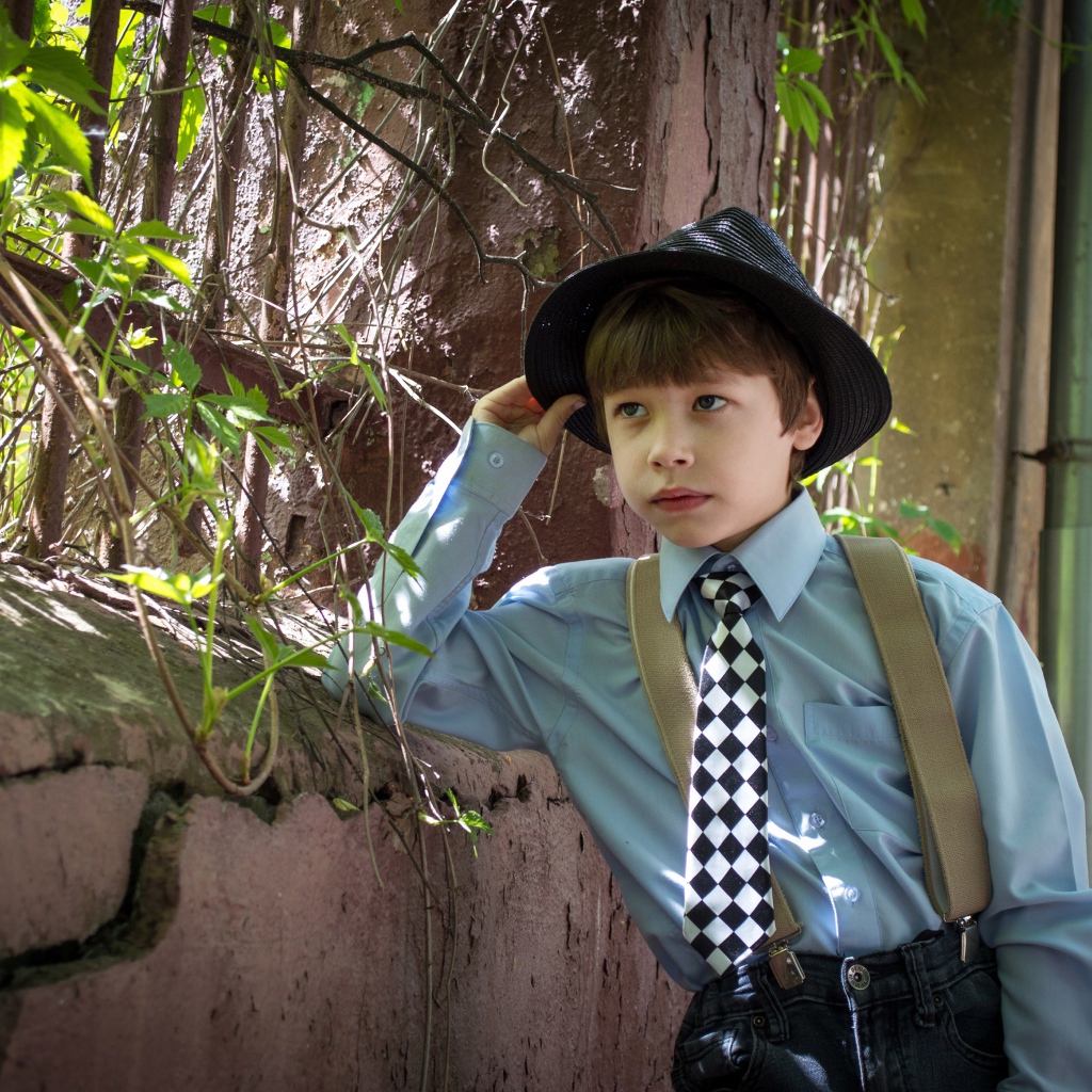 Красивый мальчик в шляпе стоит у забора 