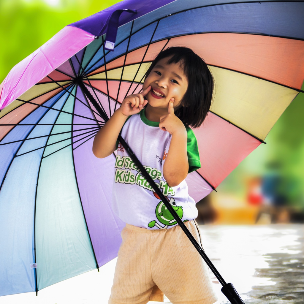 Маленькая девочка азиатка под большим разноцветным зонтом 