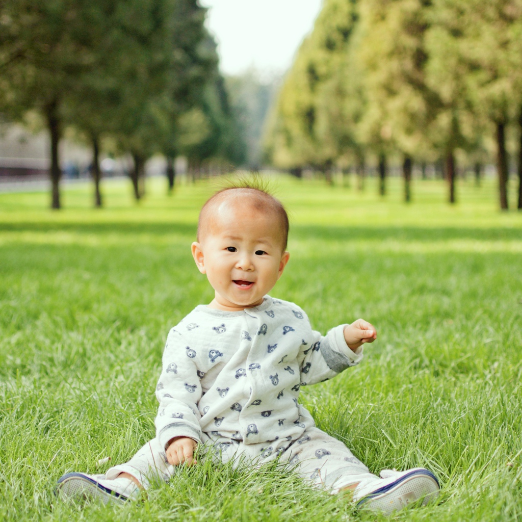 Маленький ребенок азиат сидит на зеленой траве 