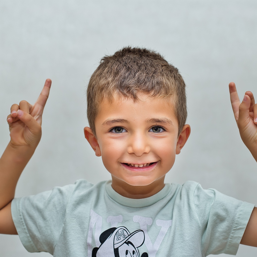 Маленький мальчик поднял руки вверх на сером фоне