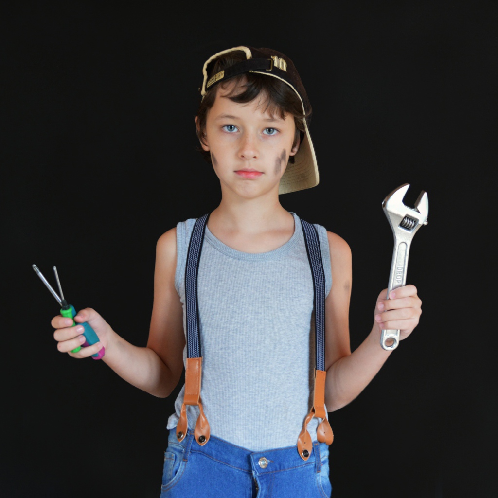 Маленький мальчик с инструментами в руках на черном фоне