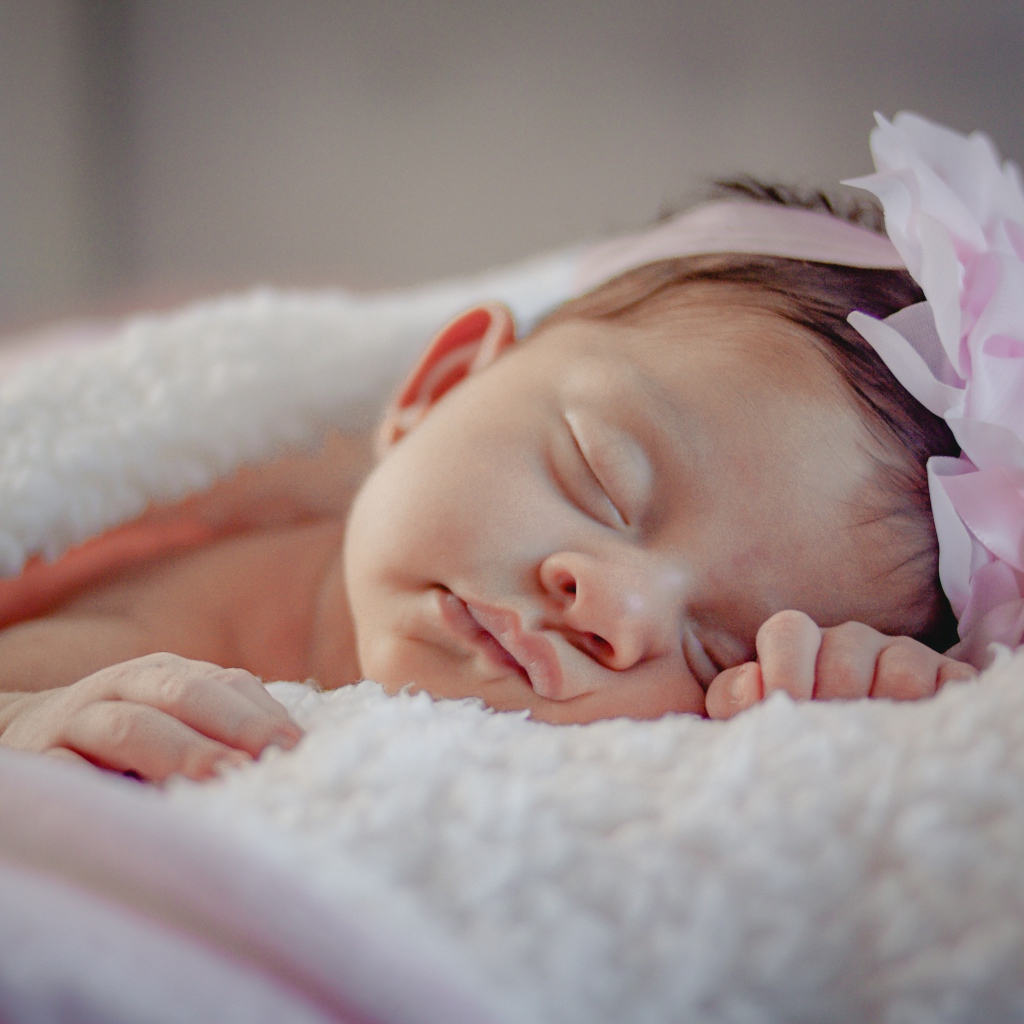 Маленькая грудная девочка с цветком на голове на кровати 