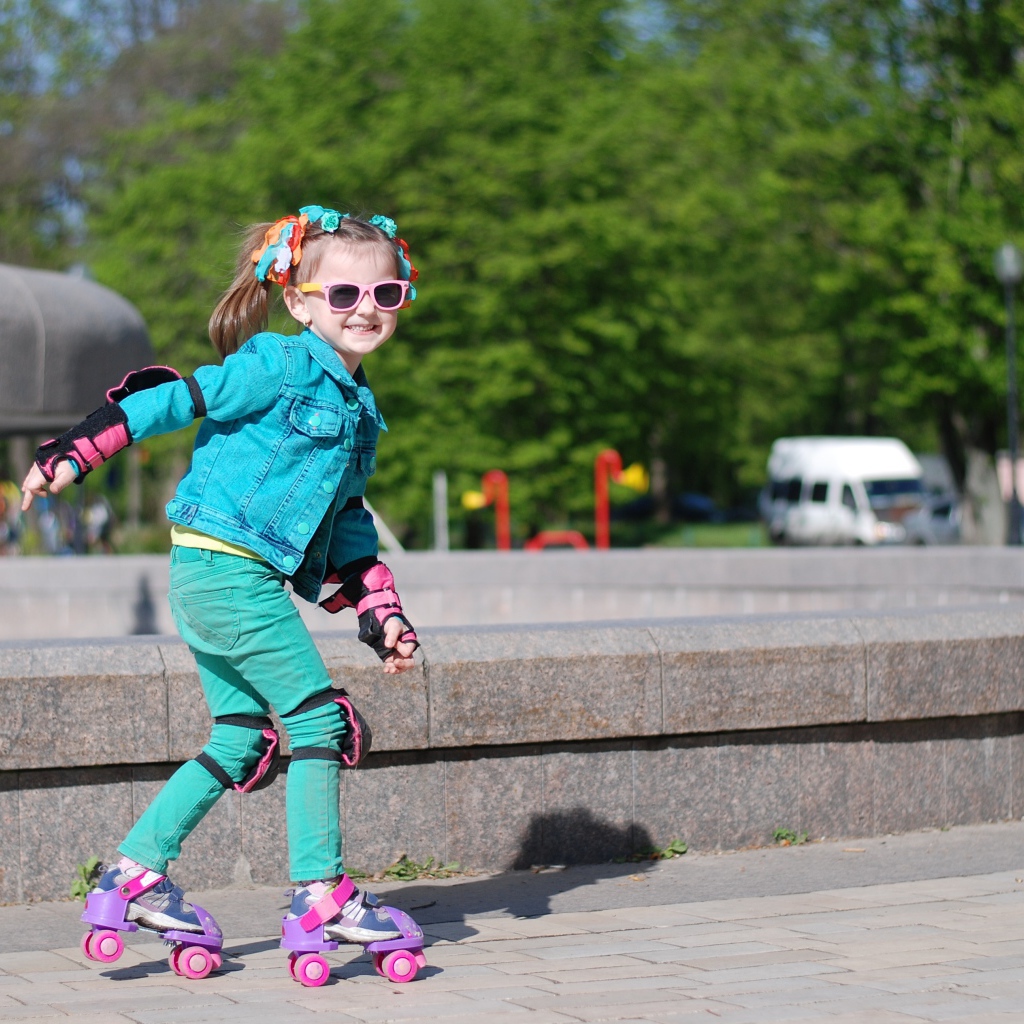 Маленькая веселая девочка катается на роликах