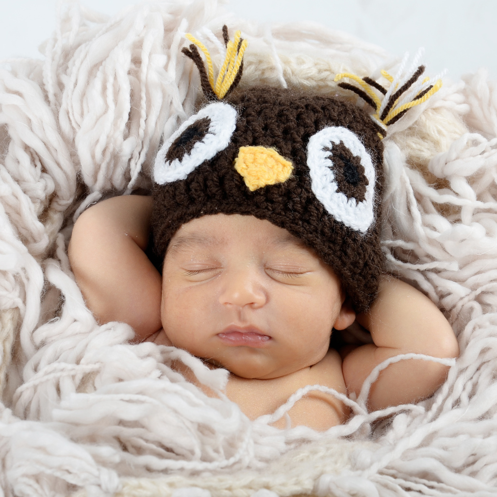 Маленький ребенок  в вязаной шапке спит на кровати 