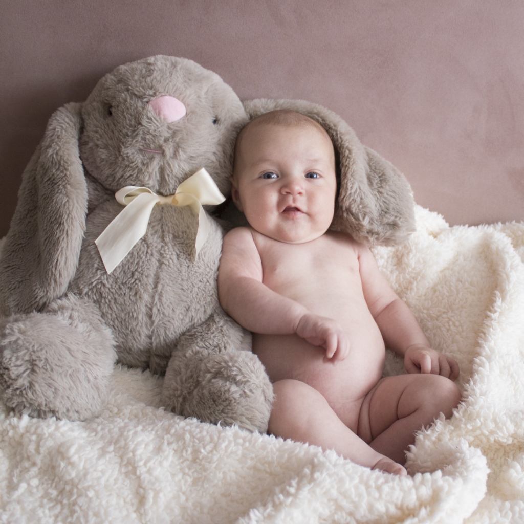 Маленький ребенок с игрушкой сидит у стены