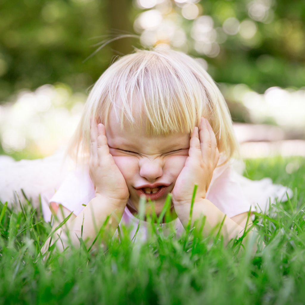 Маленькая смешная девочка лежит на зеленой траве 