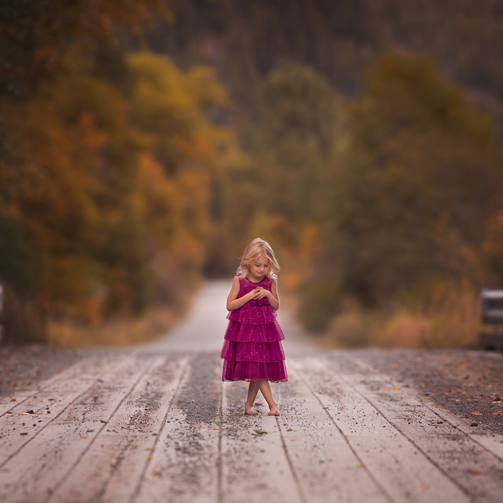 Маленькая девочка в платье стоит на мосту 