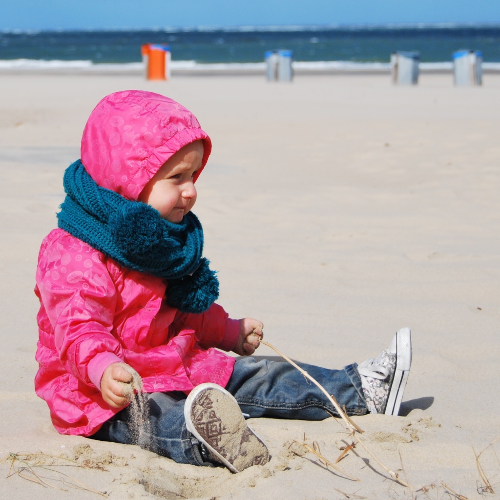 Маленькая девочка в розовой куртке на песке