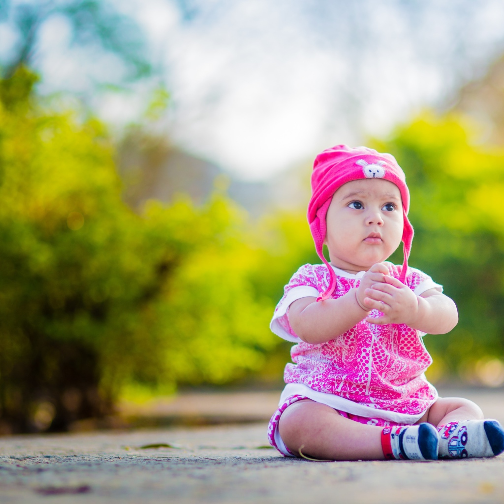 Маленькая девочка в розовом костюме сидит на земле