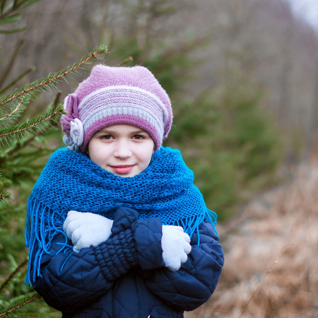 Маленькая девочка в теплой одежде у ели