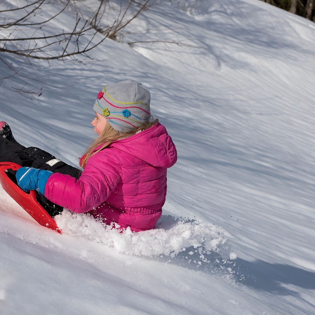 Маленькая девочка катится с заснеженной горки 