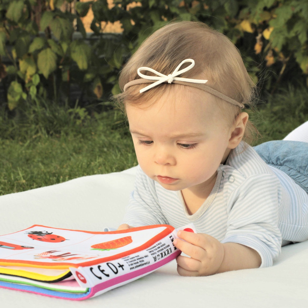 Маленькая девочка лежит на покрывале с книгой