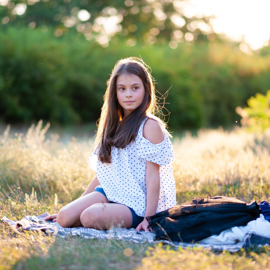 Маленькая девочка сидит на покрывале на земле 