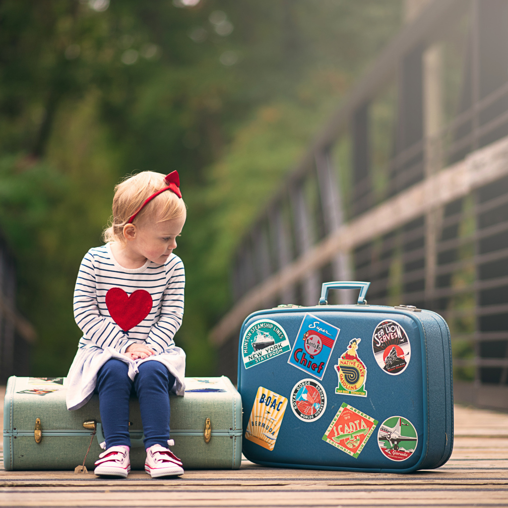 Маленькая девочка сидит на мосту с чемоданами