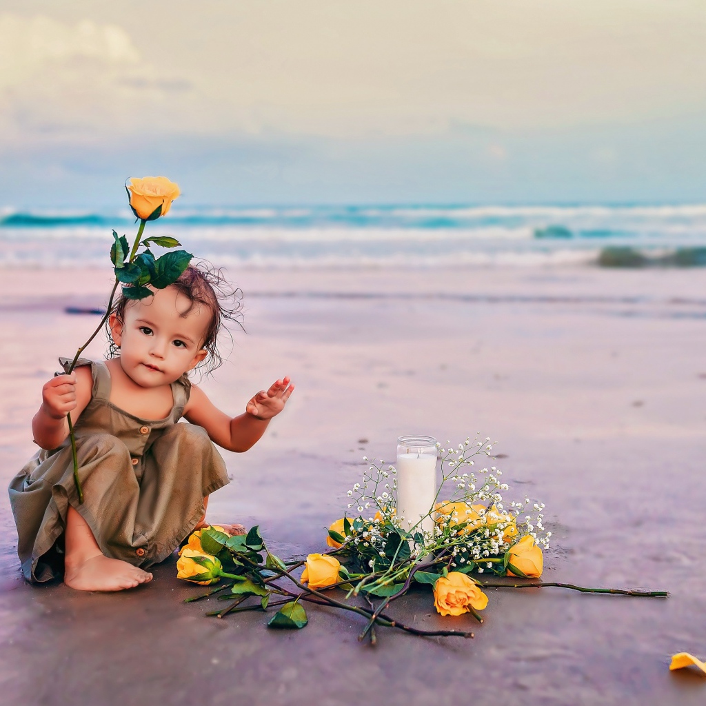 Маленькая девочка сидит на песке с розами 