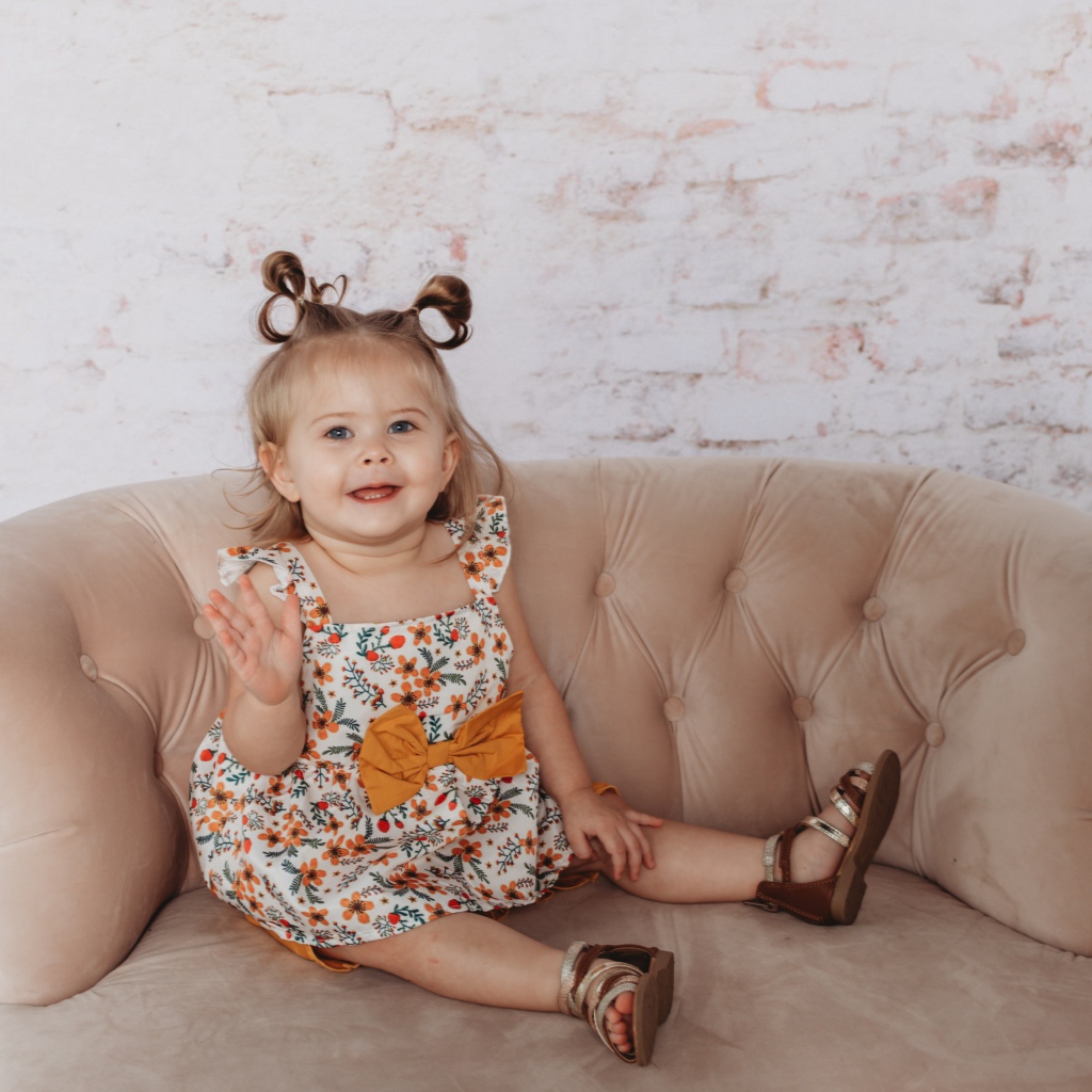 Маленькая девочка сидит на диване у стены