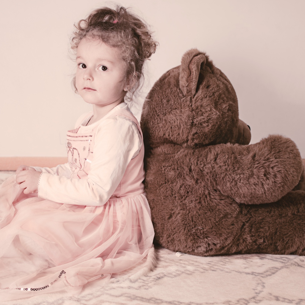 Маленькая девочка сидит с большим медведем