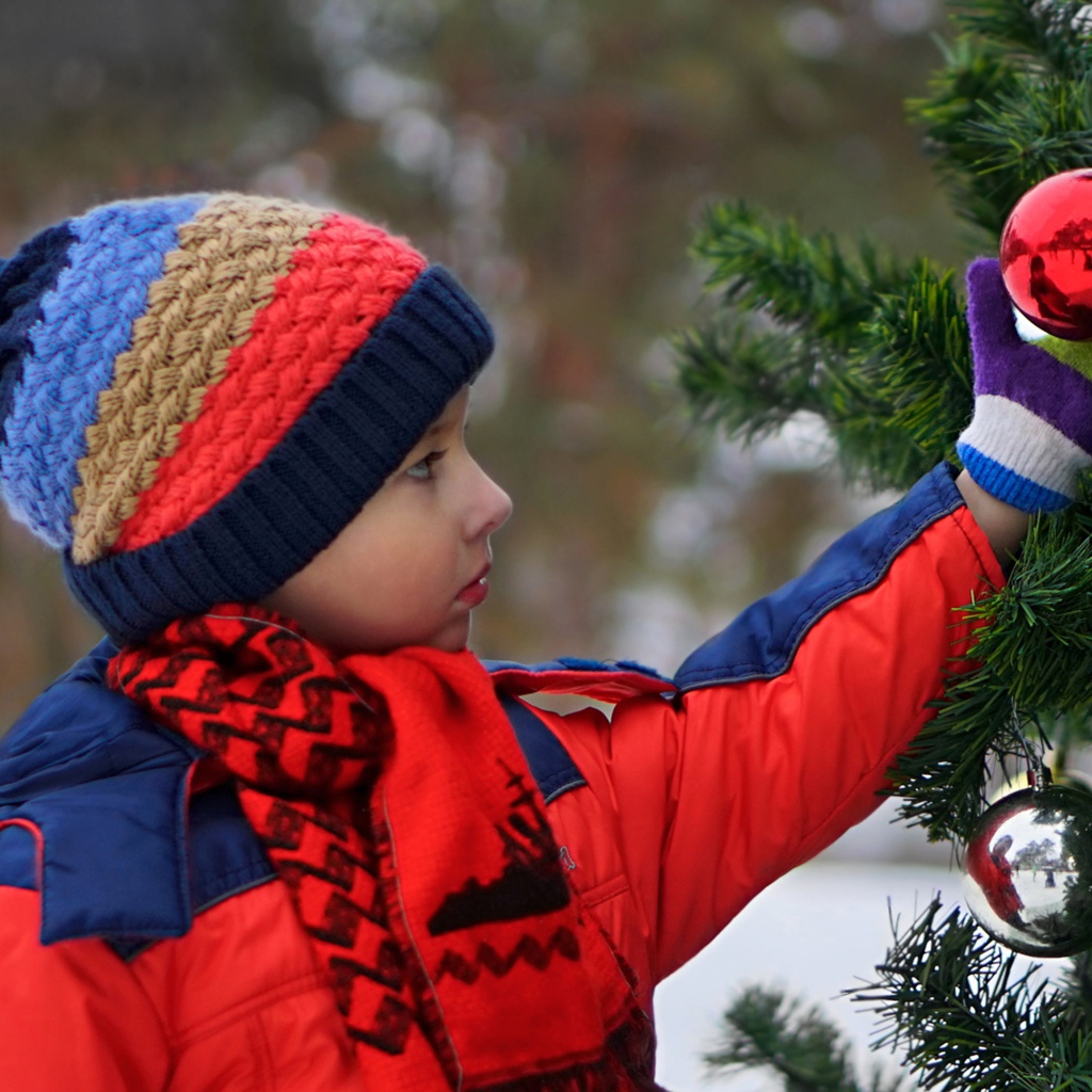 Маленькая девочка снимает красный шар с елки 