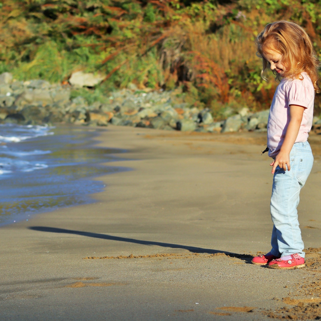 Маленькая девочка гуляет по мокрому песку 