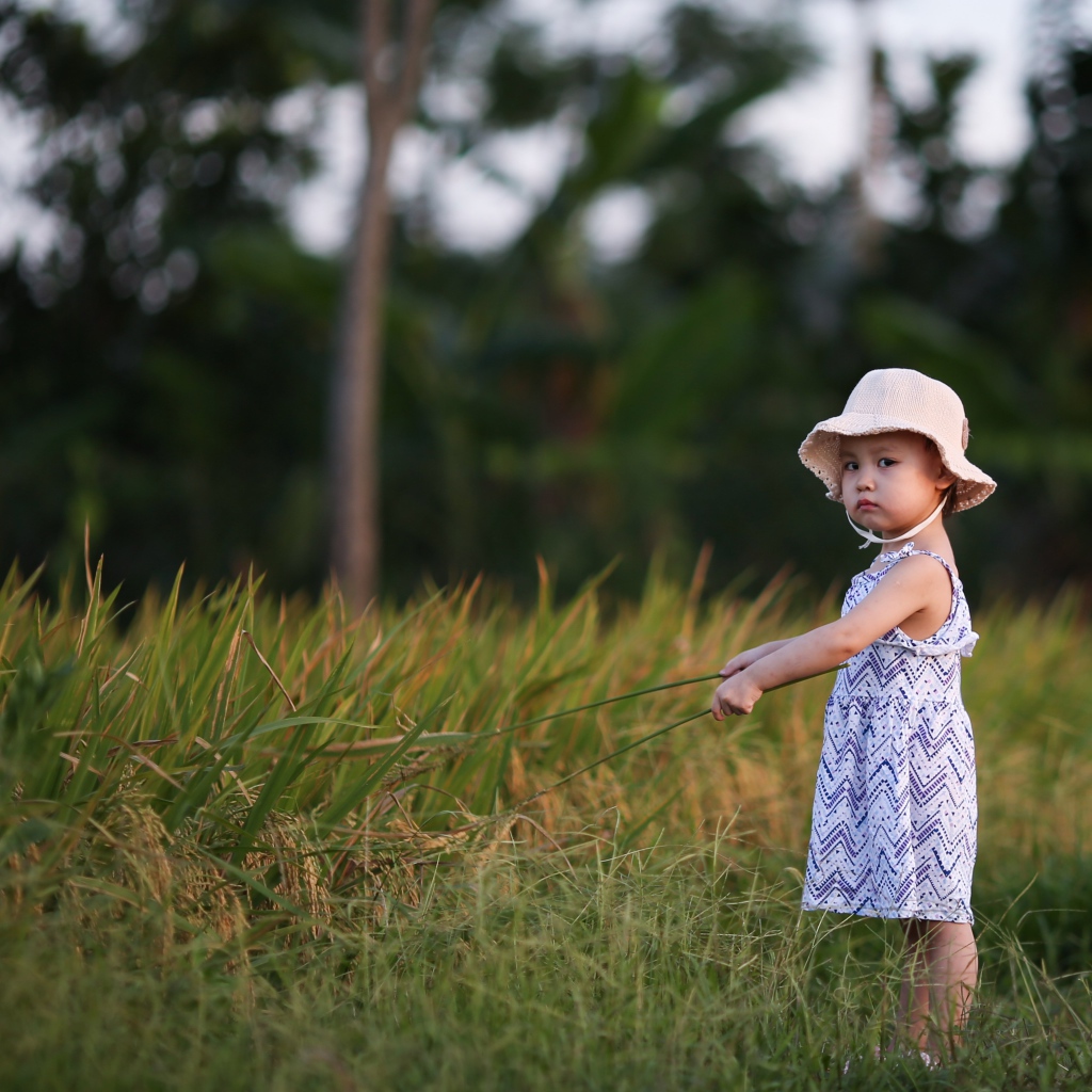 Маленькая девочка с панамой на голове  стоит в траве