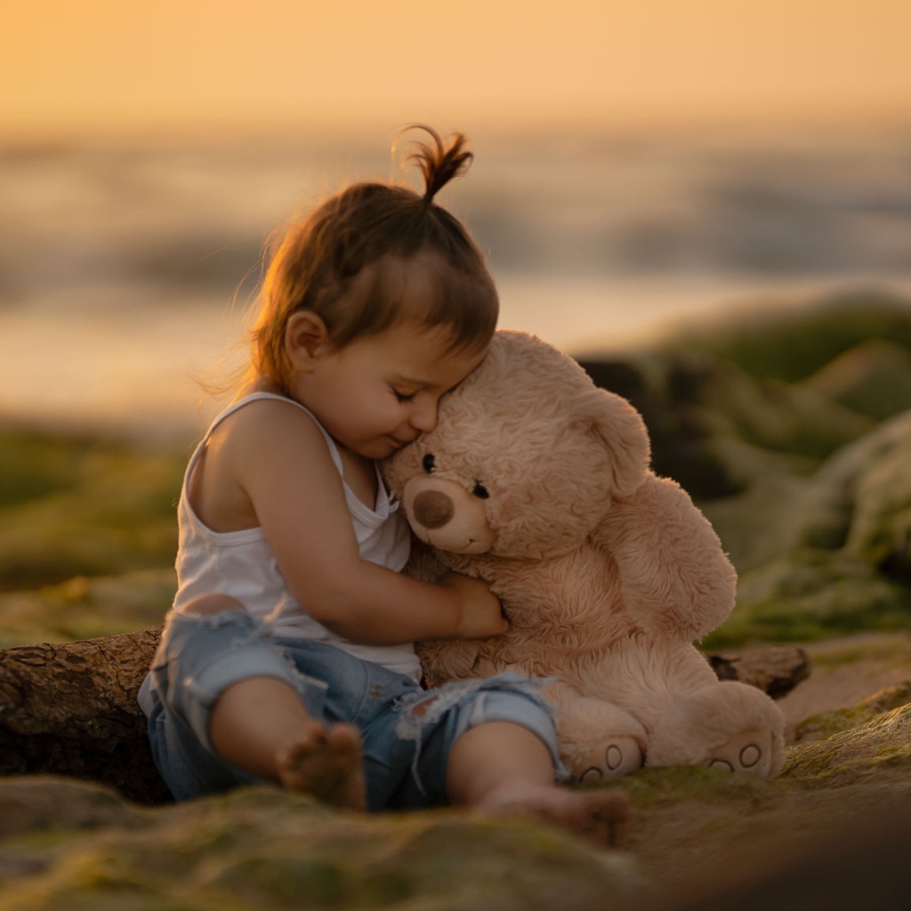 Маленькая девочка с игрушечным медведем сидит на камне