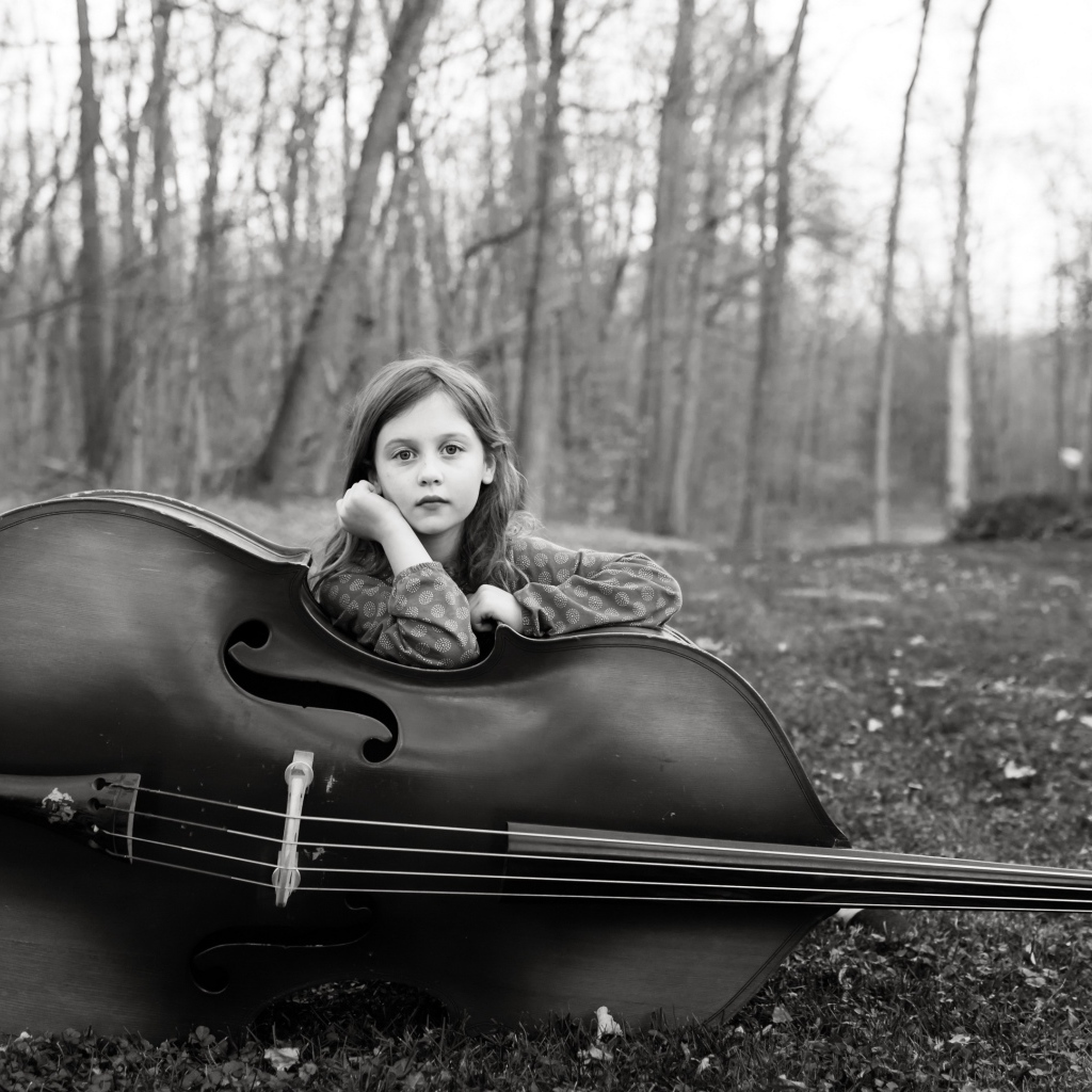 Маленькая девочка с виолончелью сидит в парке