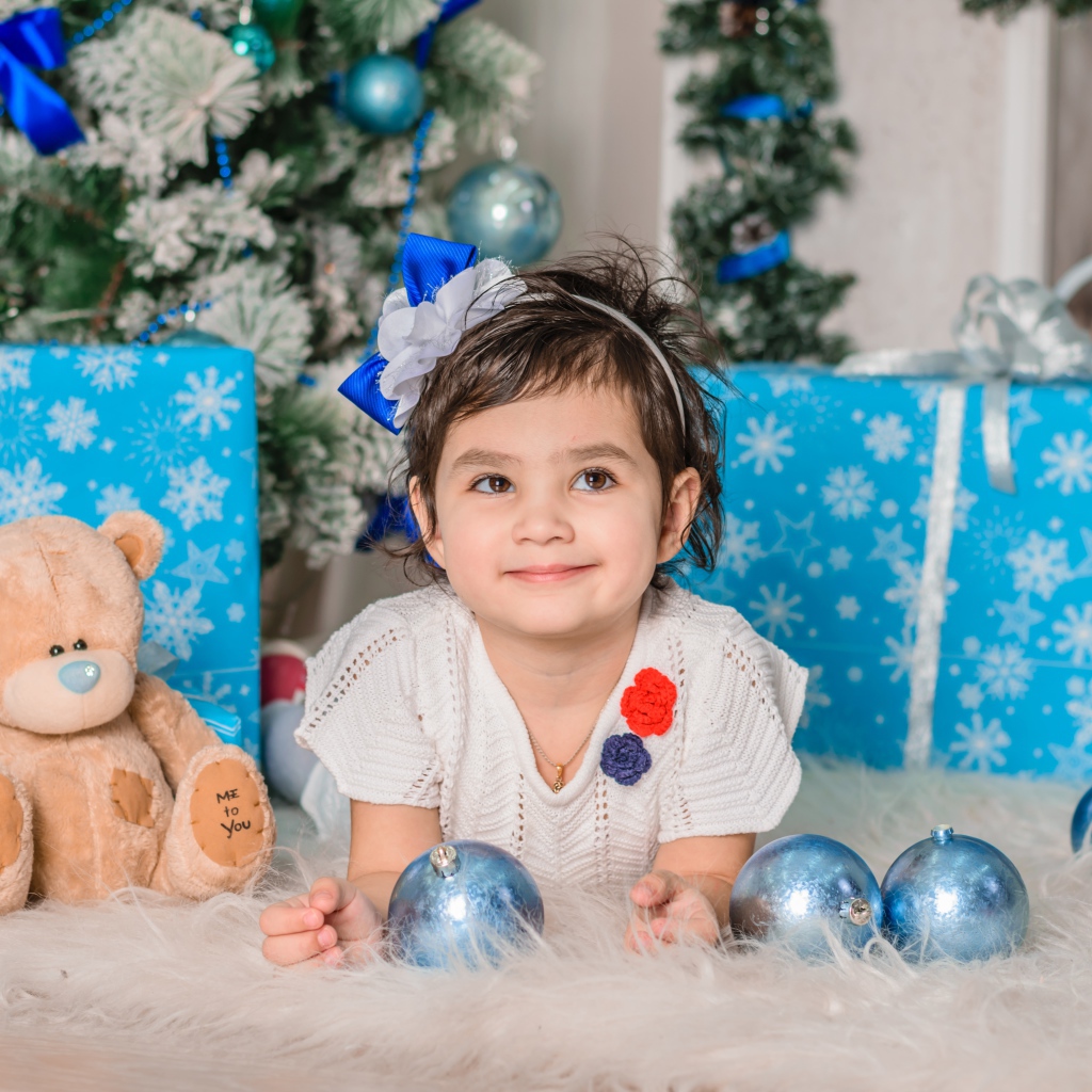 Маленькая девочка с подарками и игрушками под елкой 
