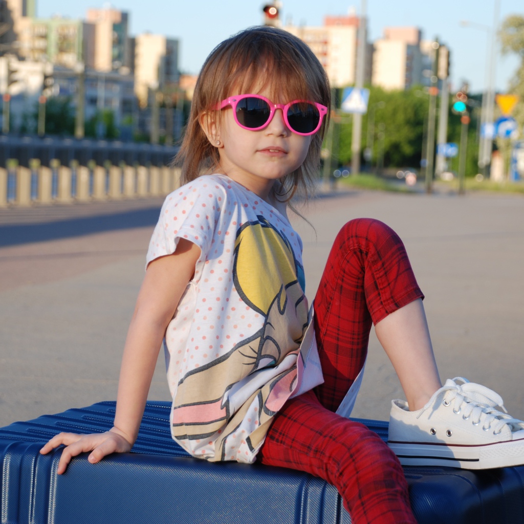 Маленькая девочка в очках сидит на чемодане