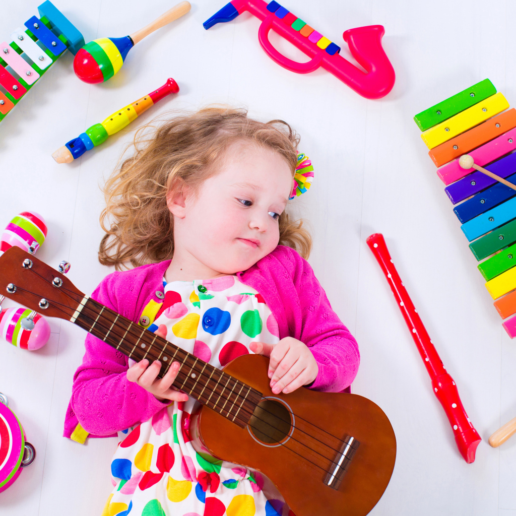 Маленькая девочка с гитарой и игрушечными музыкальными  инструментами 