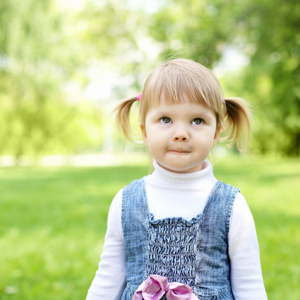 Маленькая девочка с хвостиками на голове в парке 