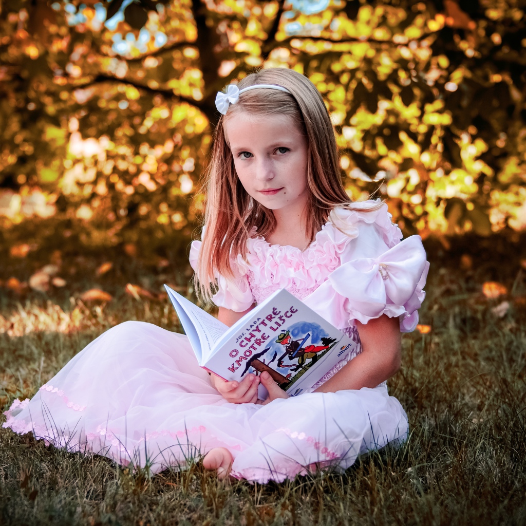 Маленькая принцесса сидит на траве с книгой