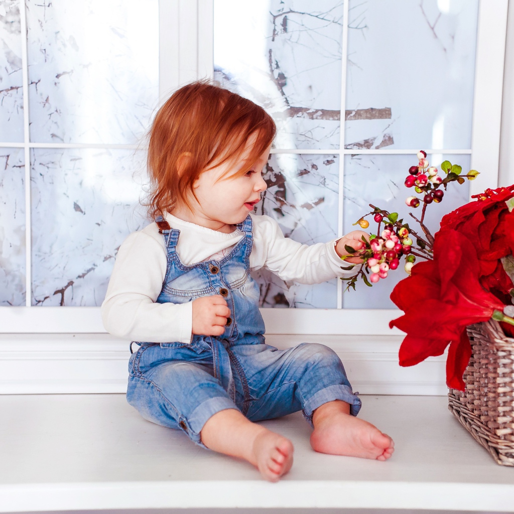 Маленькая рыжеволосая девочка сидит у корзины цветов 