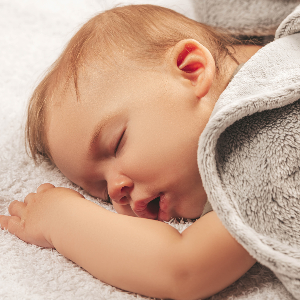 Маленький спящий ребенок под серым покрывалом 